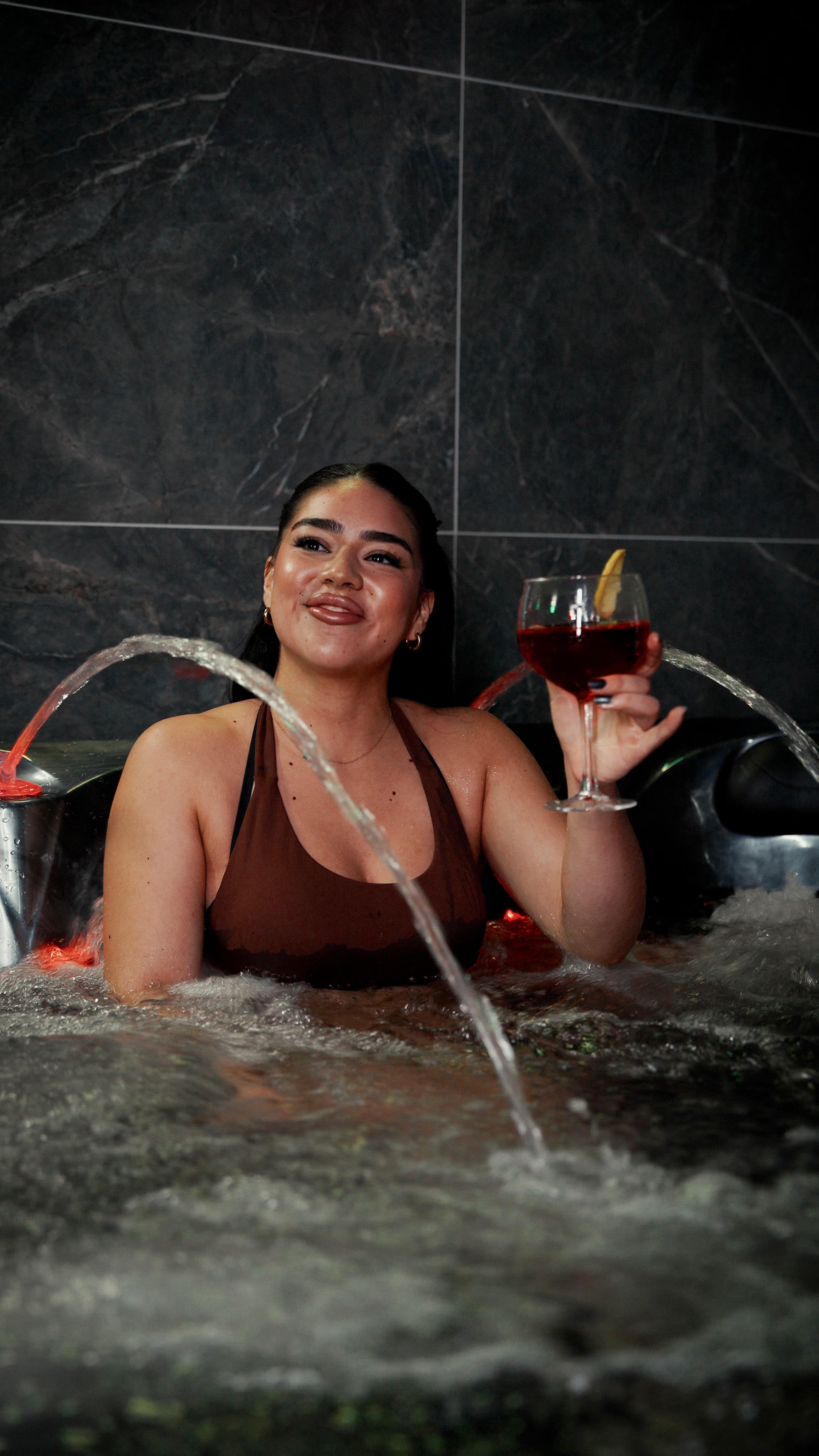 Gast ontspant in de luxe jacuzzi bij OM Cinema & Spa — rode accentverlichting en marmer